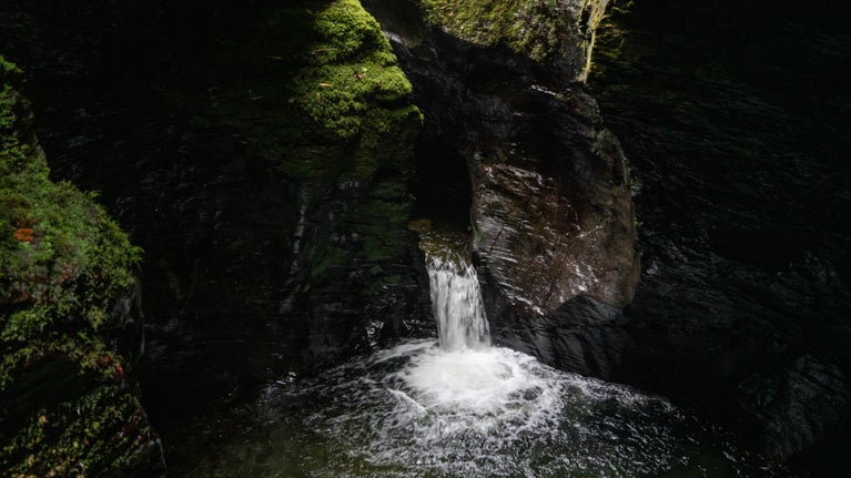 View of the River Lyd flowing through a narrow slit in the rock walls of Lydford Gorge and foaming white in the Devil's Cauldron